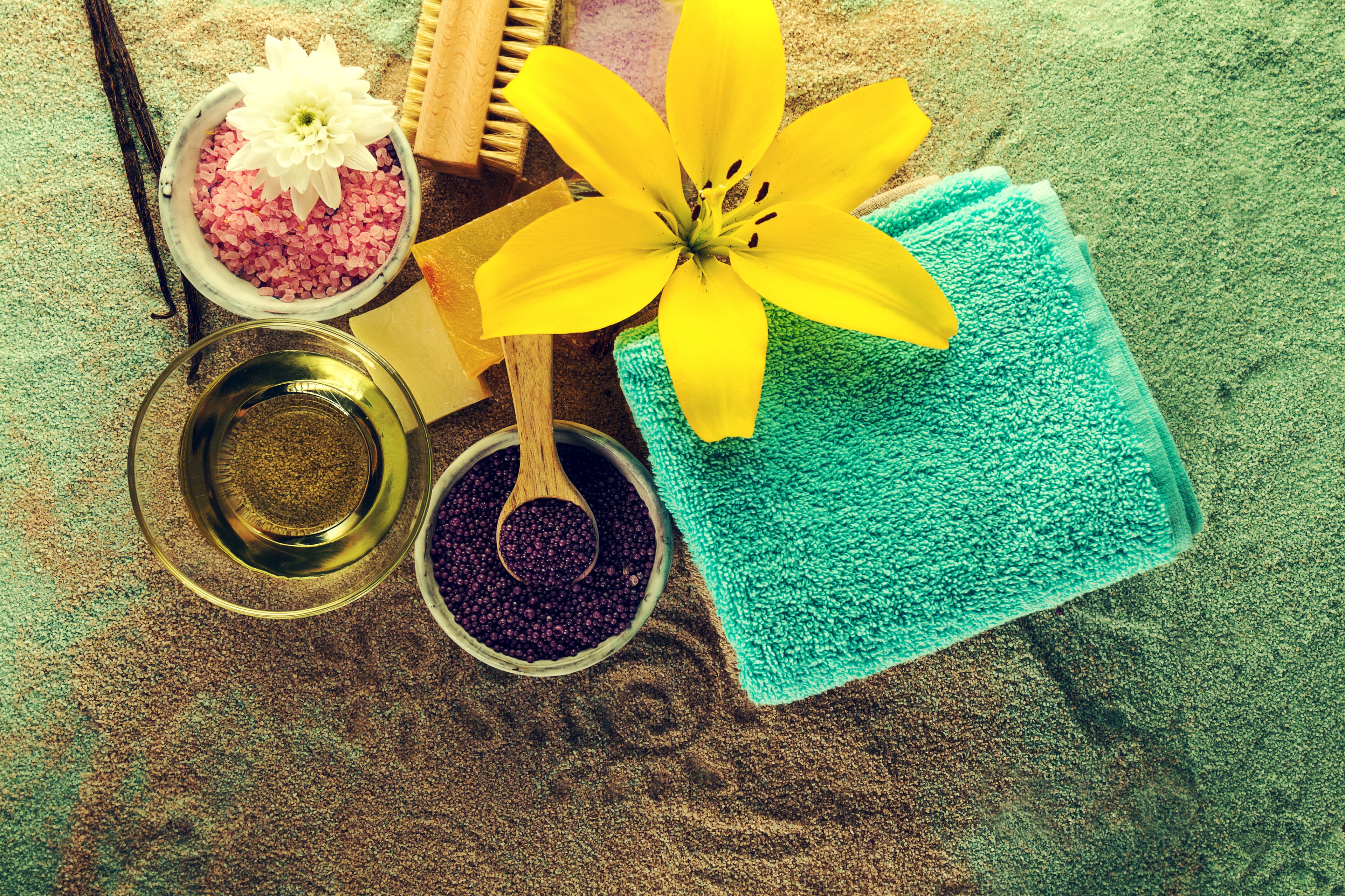 Ayurvedic ingredients — herbal oils, salts and flowers — arranged on a sand backdrop.